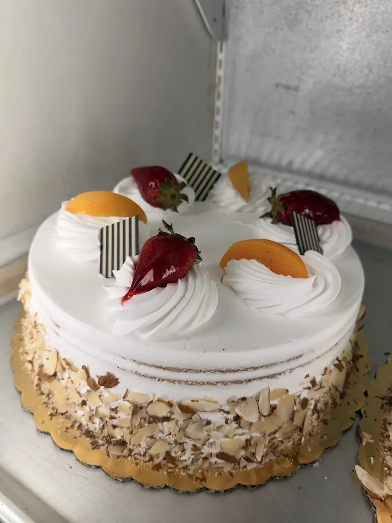 A cake with whipped cream, strawberries, peaches and sliced almonds in the panadería case